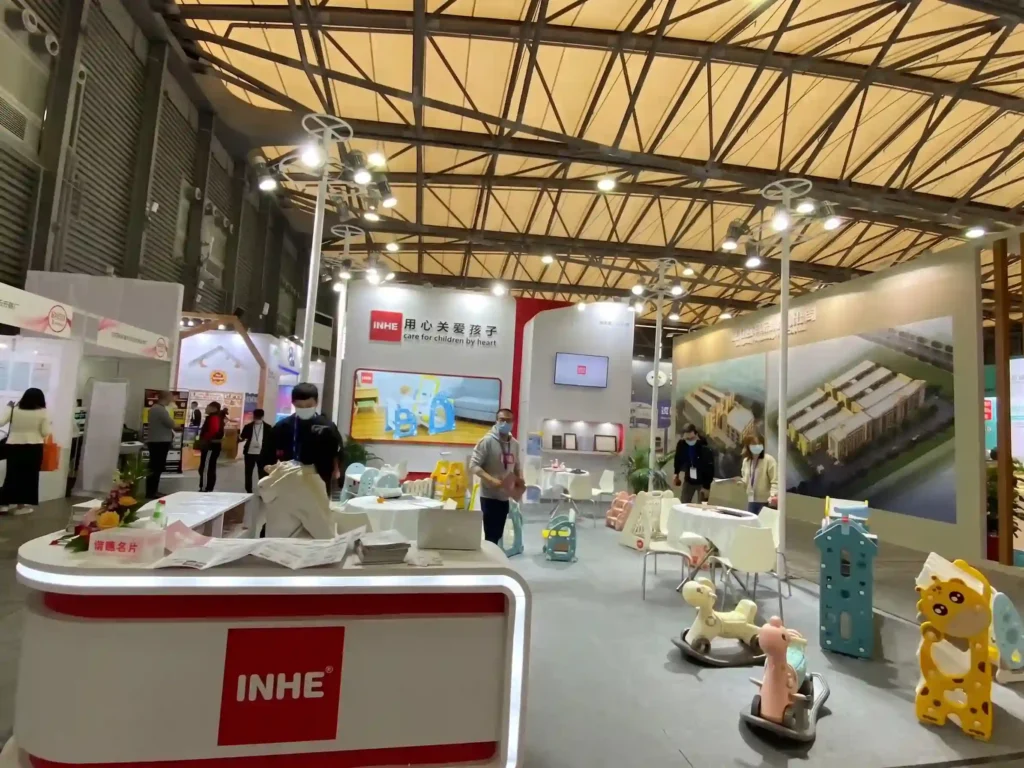 A wide-angle view of the modern Inhe exhibition pavilion at China Toy Expo, showcasing a sleek reception desk and premium preschool educational equipment.