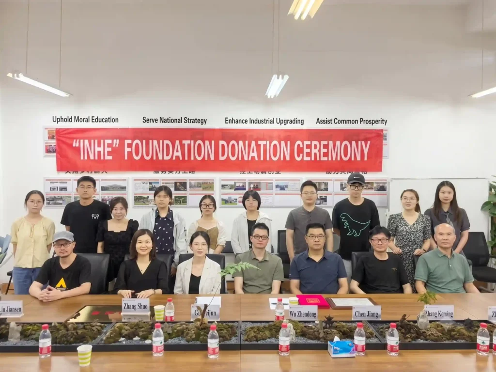 Large group photo of attendees at the "Inhe" Foundation Donation Ceremony, with a red banner hanging in the background.