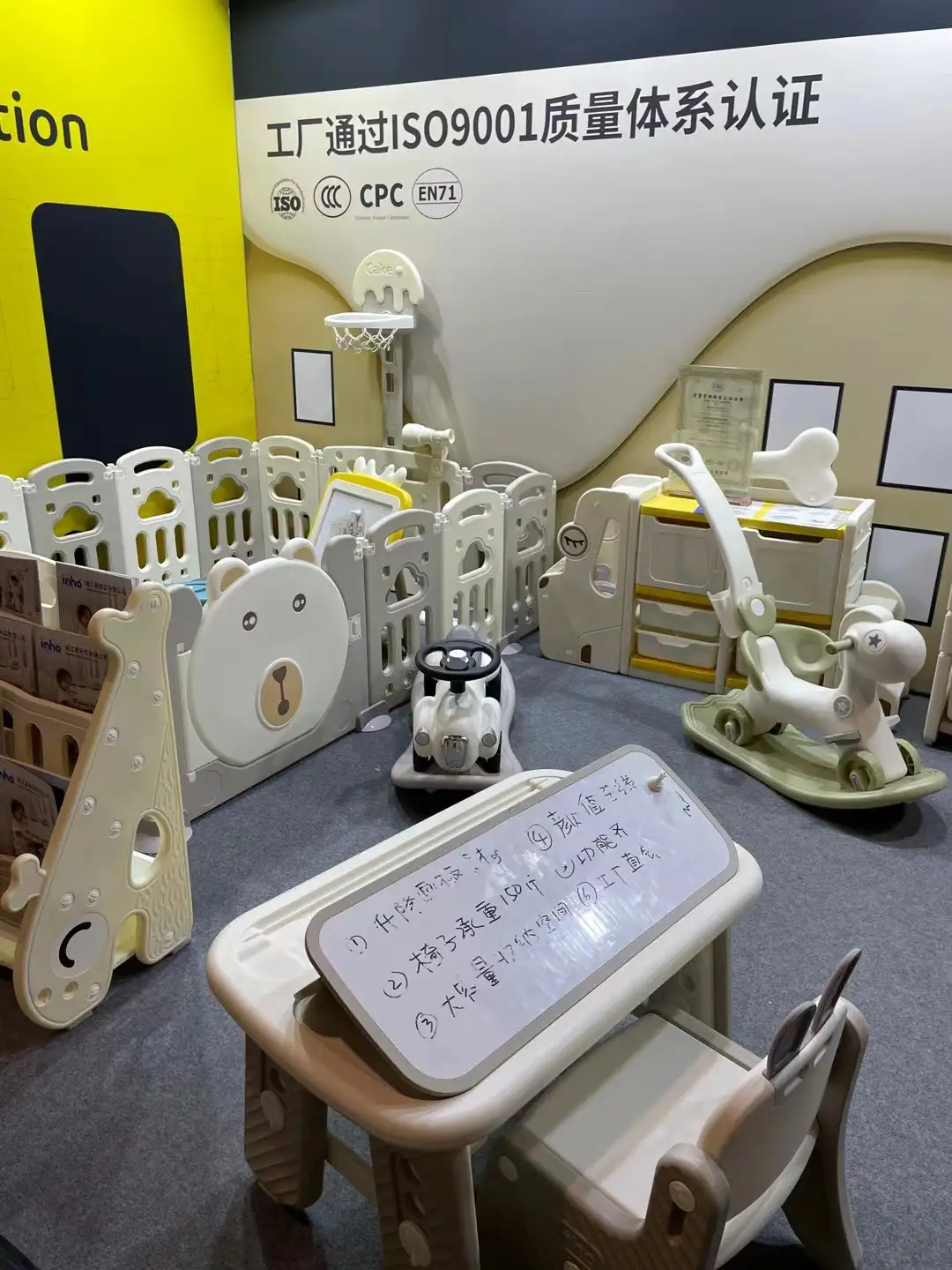 A showroom display featuring a bear-themed children's modular plastic playpen, indoor basketball hoop, activity desk set, and giraffe-shaped organizer rack.