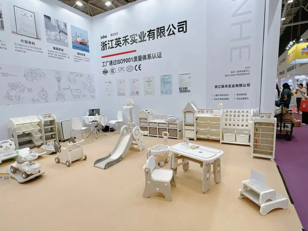 A full view of the Inhe booth showroom showcasing minimalist cream feeding cabinets, house-shaped toy organizers, activity tables, and indoor slides.