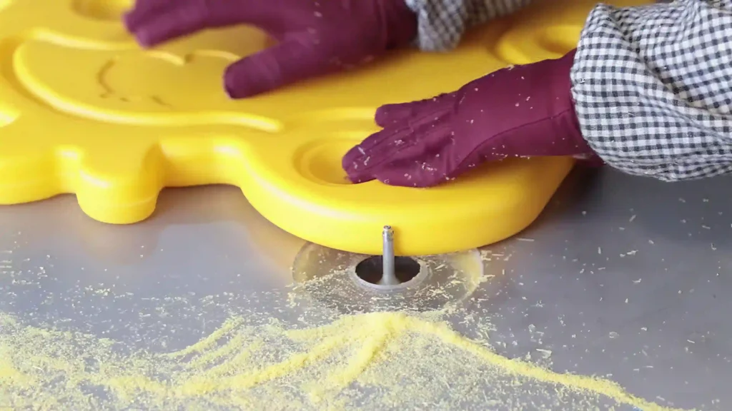 Worker manually trimming a yellow molded plastic component.